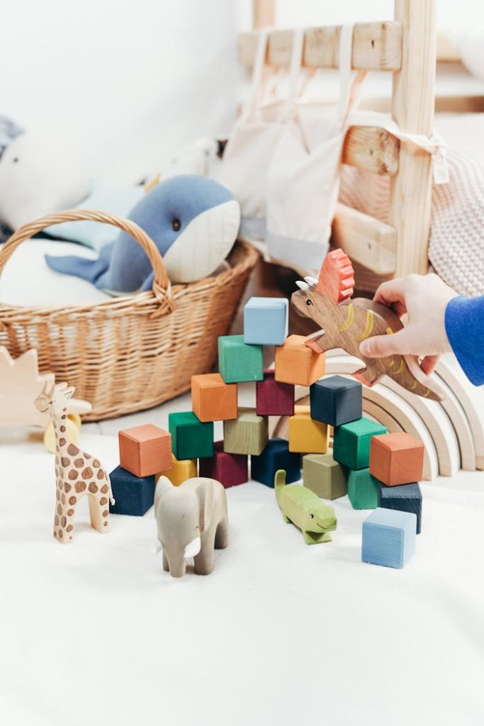 A childs hand arranges colorful wooden toys and animal figures on a playroom floor.